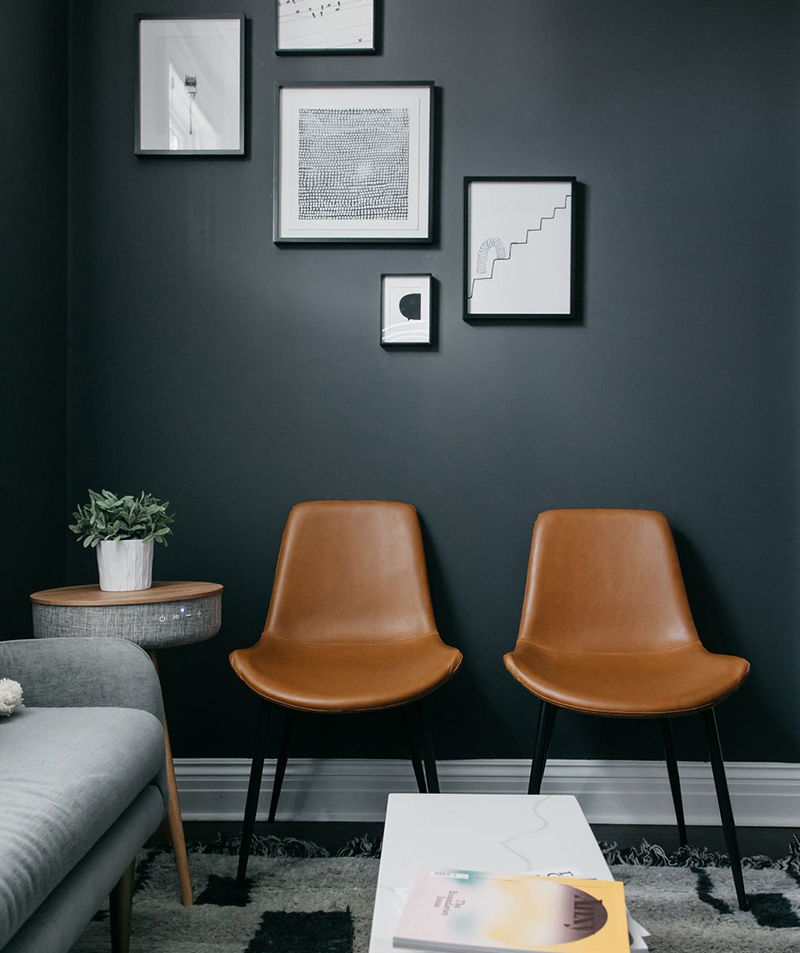Two brown chairs sitting against a dark grey wall. Participating in Therapy for Anxiety can help manage physical and mental symptoms.