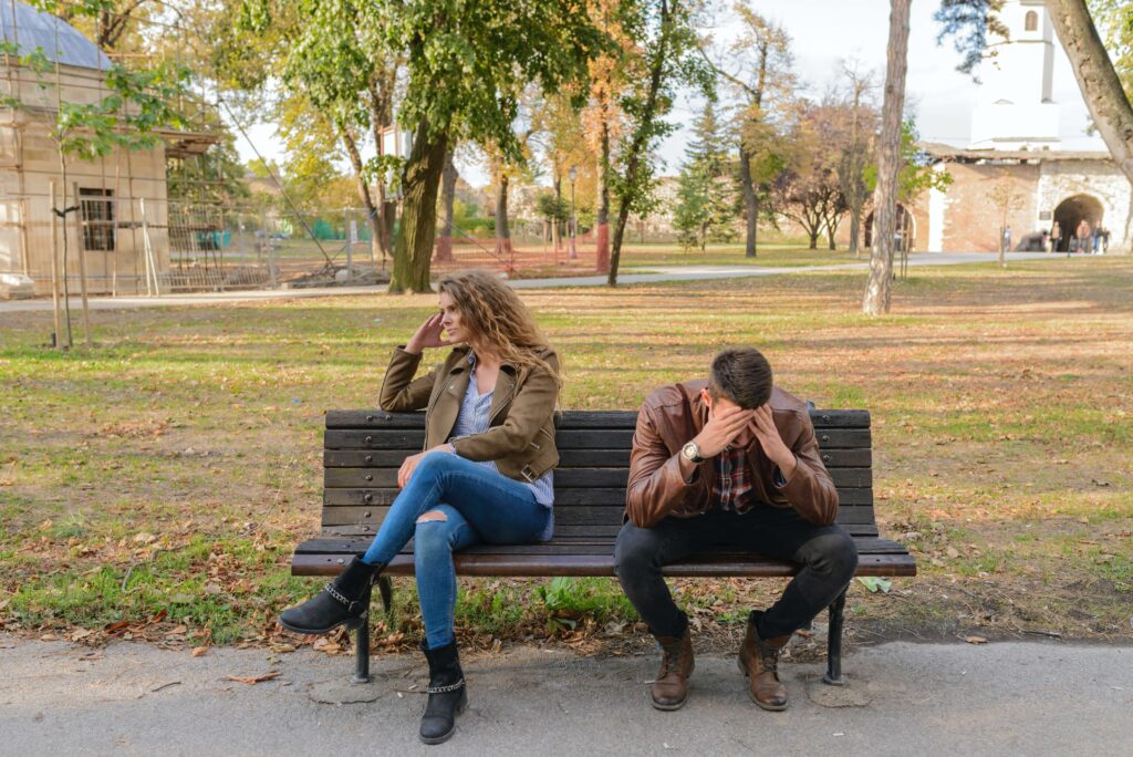A couple sits facing away from each other on a park bench representing a couple that could benefit from working with a couples therapist for couples conflict resolution in Burbank, CA.