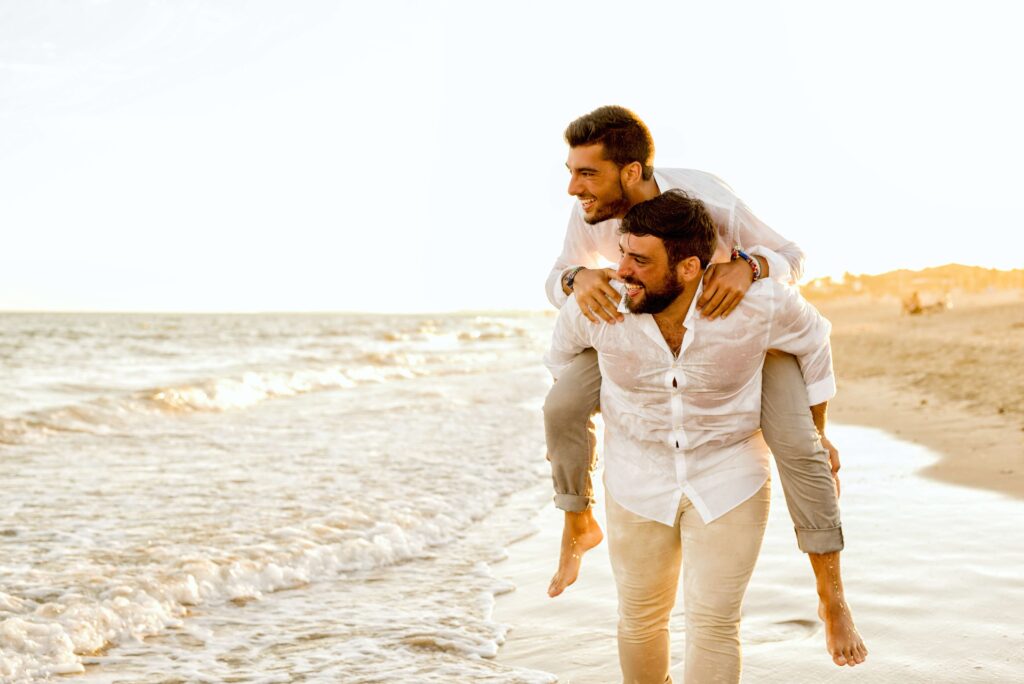 A man gives his partner a piggyback ride on the beach representing the depth of connection that can be obtained in Couples Counseling in Burbank, CA.