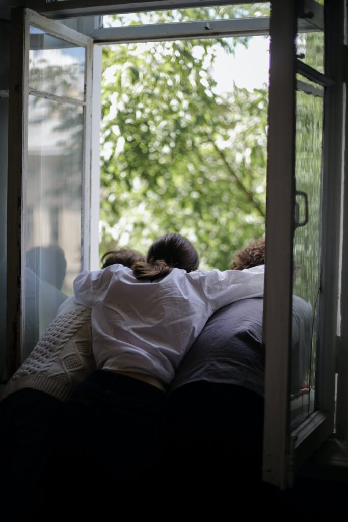 A threesome looks out a window with their arms around each other representing the bond that can be formed in an open relationship in Burbank, CA.