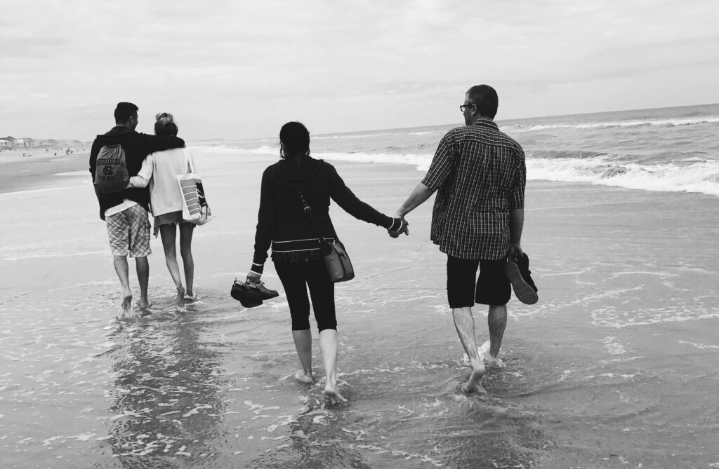 Two couples in black and white, walking on the shoreline representing the improved connection that can be fostered through Therapy for Couples in Burbank, CA.