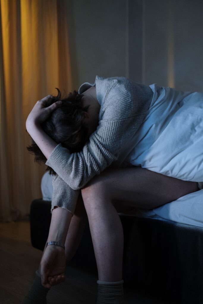 An individual sits in a dark room on the edge of their bed with their head down representing the need for Therapy for Anxiety in Burbank, CA.
