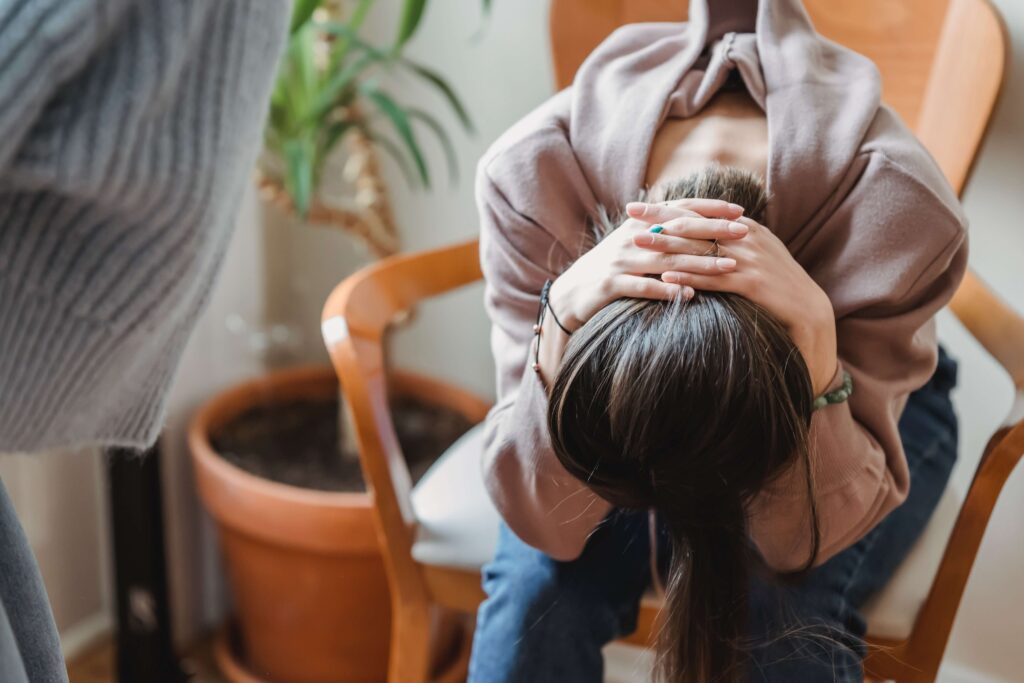 A woman struggling with perfectionism sits with her head down and her hands clenched behind her neck representing someone who could benefit from Therapy for Anxiety in Burbank, CA.
