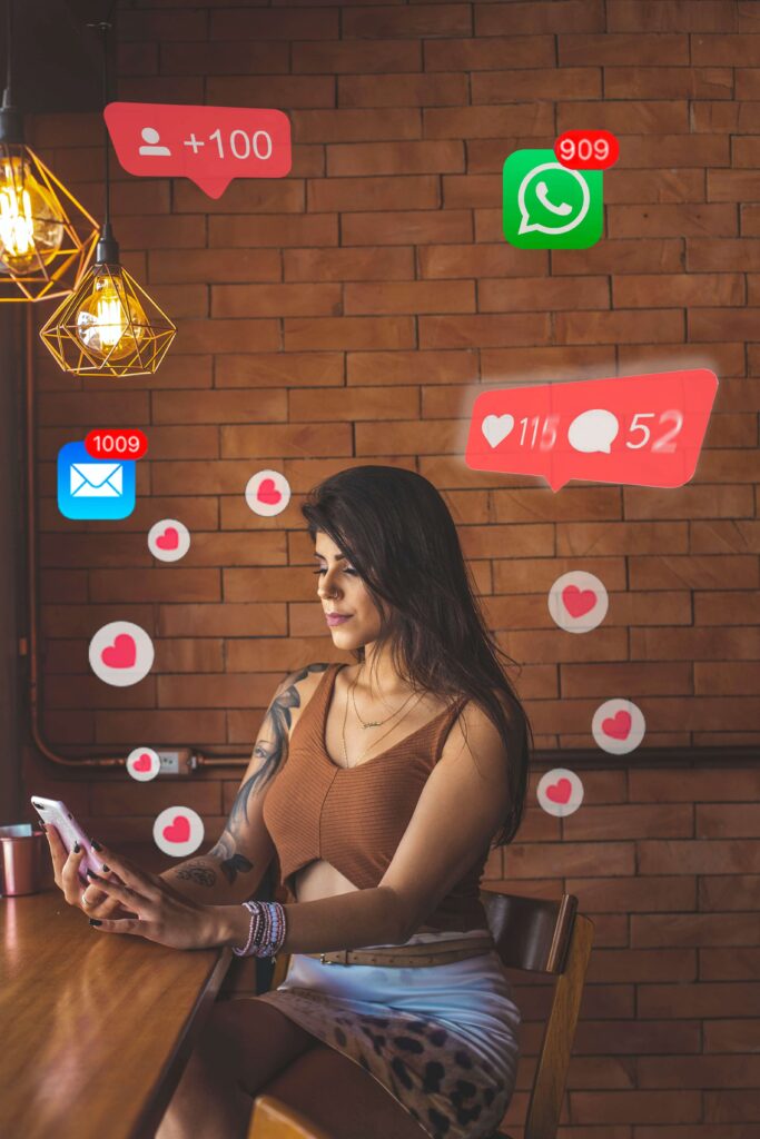 A young woman sits at sits on her phone surrounded by various social media emojis representing someone who is overwhelmed by social media anxiety in Burbank, CA.