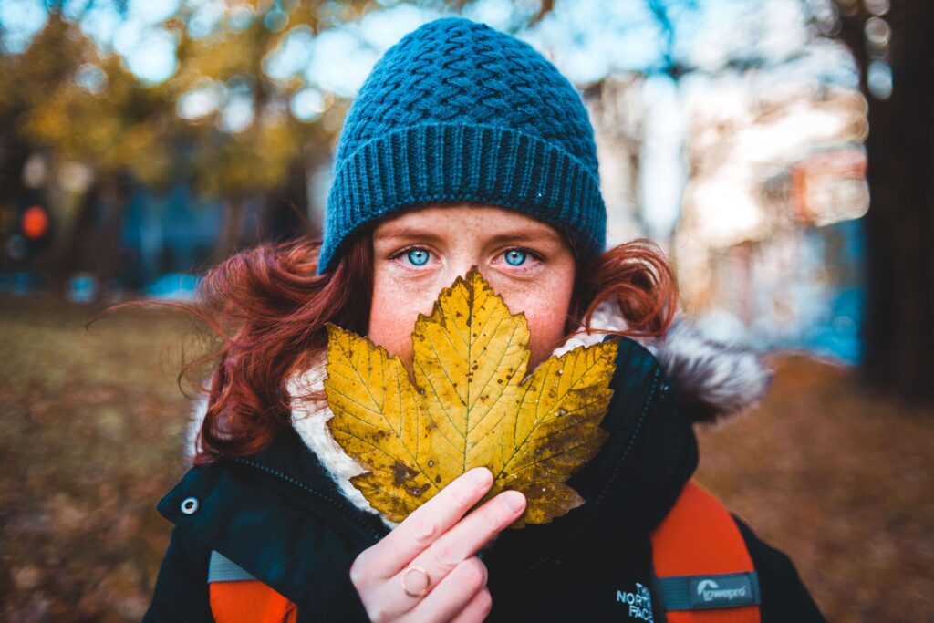 A woman in a blue beanie holds a fall leaf in front of her face representing someone who is hiding from the world due to SAD. Get support during this time of year in Therapy for Depression in Burbank, CA.